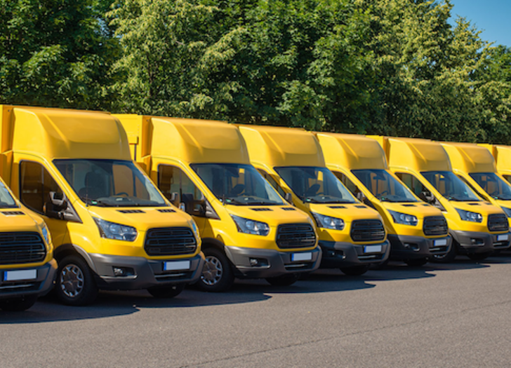 A row of bright yellow delivery trucks lined up in a parking lot.