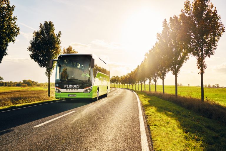A Flixbus driving on a sunny road lined with trees
