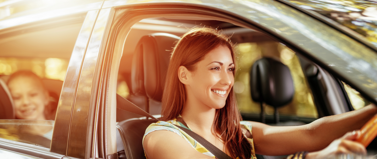 A mother driving a car with her daughter in the back seat.