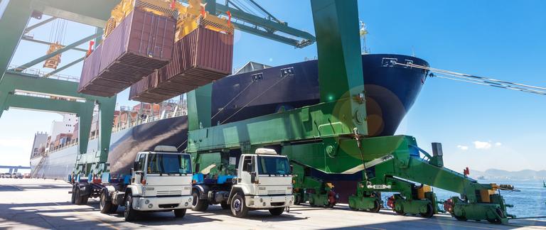 Two trucks prepare to be loaded with shipping containers at a port.