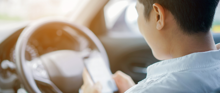 A man looks at his cell phone while sitting in the driver seat of his car.