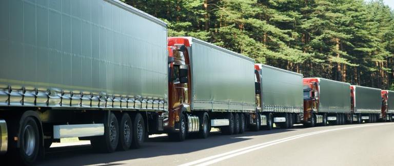 Row of trucks driving along leafy highway