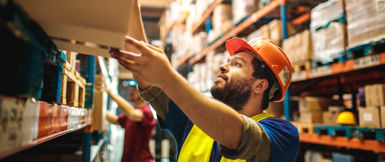 A warehouse worker lifts a box onto a shelf in a fulfilment center.