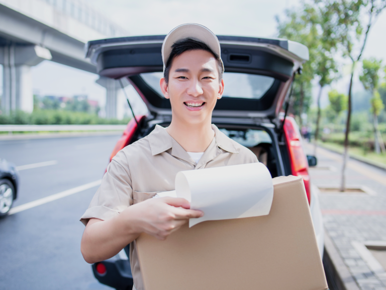 A delivery driver looks to camera, holding a package he is about to deliver.
