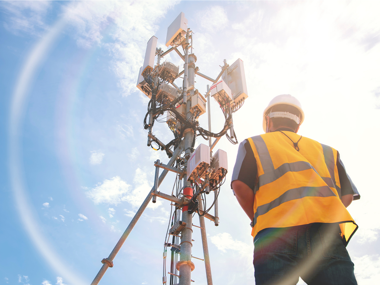 A field service worker looks up at a 5G telecoms tower antenna.