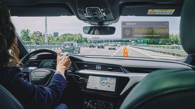 Person driving on busy highway using ISA systems and ISA technology to show a map with speed limits powered by map data.