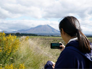 荒野でスマートフォンを片手に山の写真を取る女の子