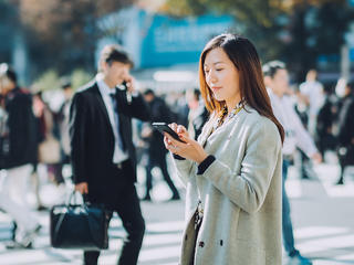街なかでスマートフォンを使いながら正確なジオコーディングで高精度位置情報を取得する女性