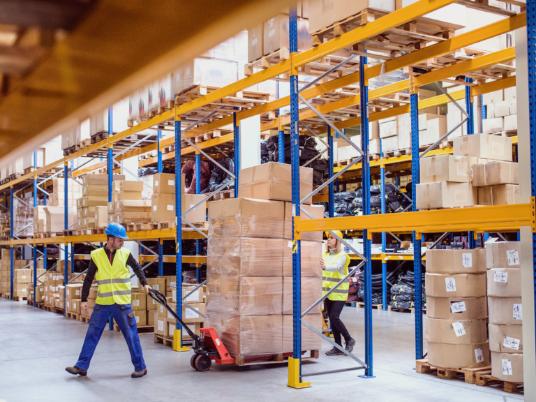 A man and a woman moving stock in a large warehouse.