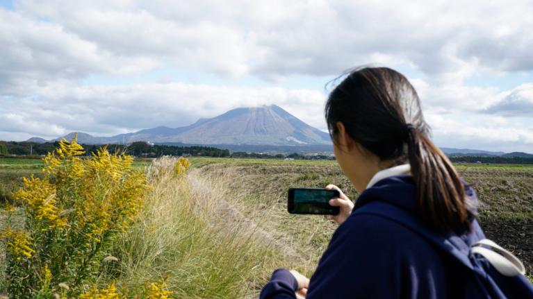 荒野でスマートフォンを片手に山の写真を取る女の子