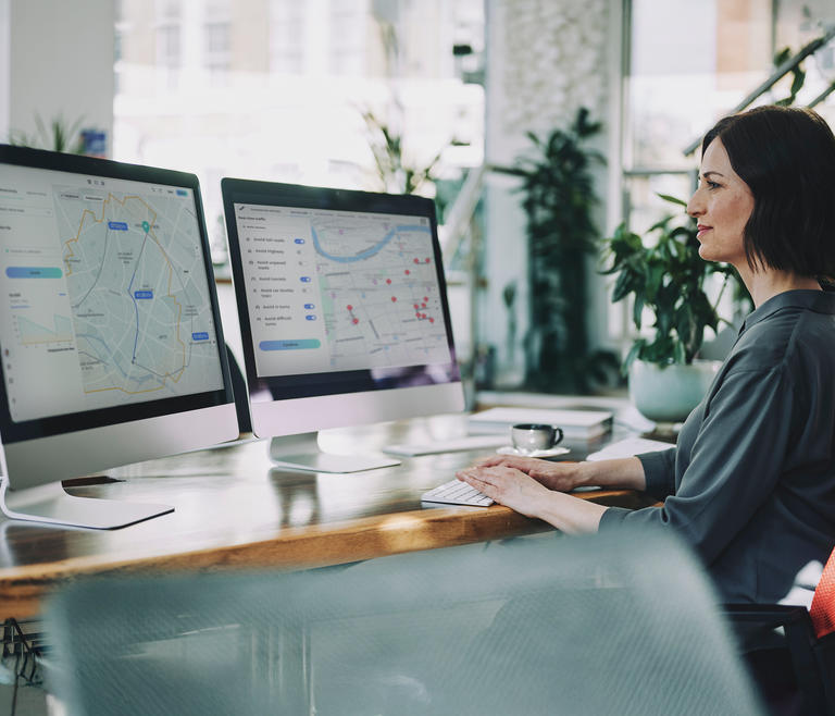 Woman sitting at desk with two monitors showing map data